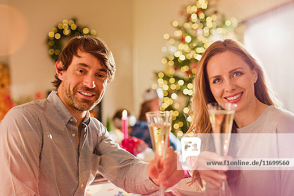 Portrait lächelndes Paar stößt mit Champagnerflöten am Weihnachtstisch an