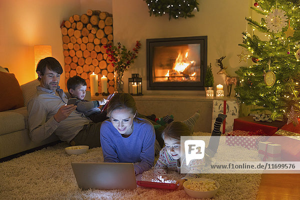 Eine Familie  die sich im weihnachtlich geschmückten Wohnzimmer mit Laptop  Tablet und Handy entspannt