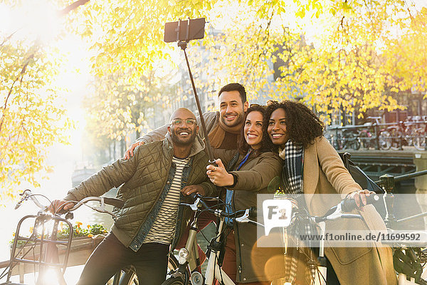 Lächelnde Freunde mit dem Fahrrad nehmen Selfie mit Selfie-Stick auf städtischer Brücke