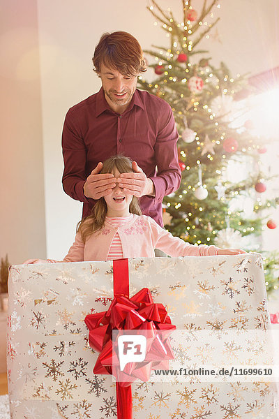 Vater bedeckt die Augen seiner Tochter  die ein großes Weihnachtsgeschenk hält