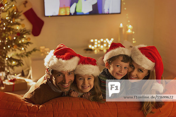Porträt einer lächelnden Familie mit Weihnachtsmannmützen auf dem Wohnzimmersofa