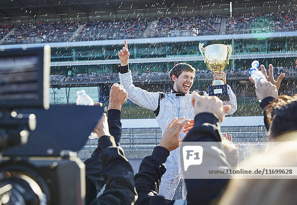 Formula one racing team spraying champagne on driver with trophy  celebrating victory on sports track