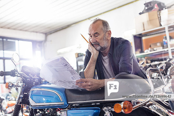 Focused Senior männlich Motorradmechaniker Überprüfung Handbuch in der Werkstatt