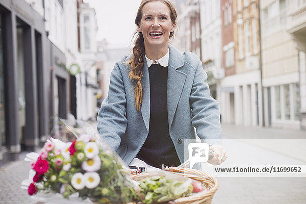 Smiling woman riding bicycle with flowers in basket