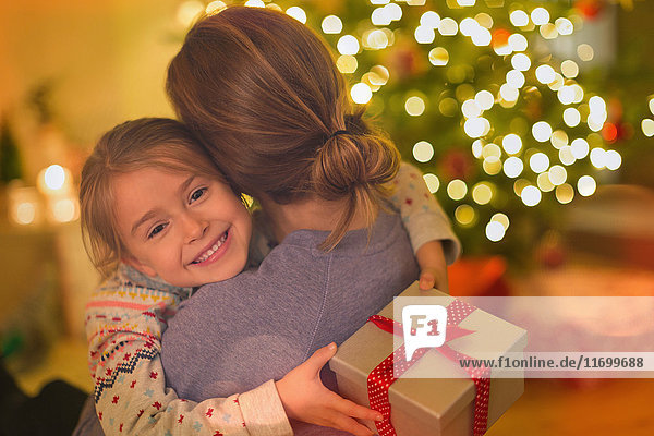 Lächelnde Tochter mit Weihnachtsgeschenk  die ihre Mutter umarmt