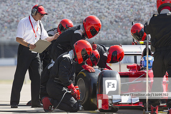 Manager with stopwatch timing pit crew replacing formula one race car tire in pit lane