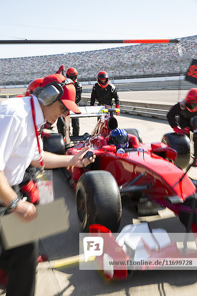Manager with stopwatch timing pit crew replacing tires on formula one race car in practice session pit lane