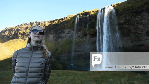 Frau mit Sonnenbrille in der Nähe eines Wasserfalls stehend