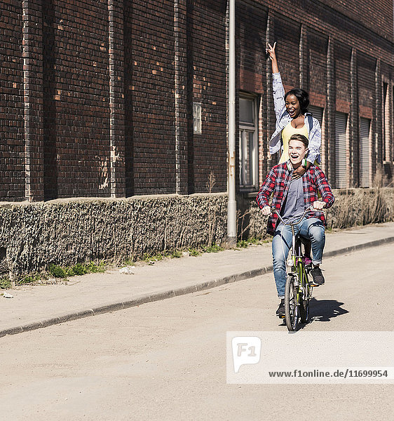 Young man riding bicycle with his girlfriend standing on rack