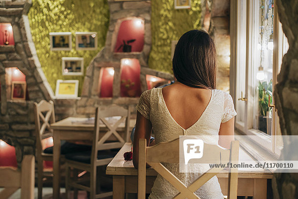 Rückansicht einer jungen Frau  die in einem Restaurant am Tisch sitzt.