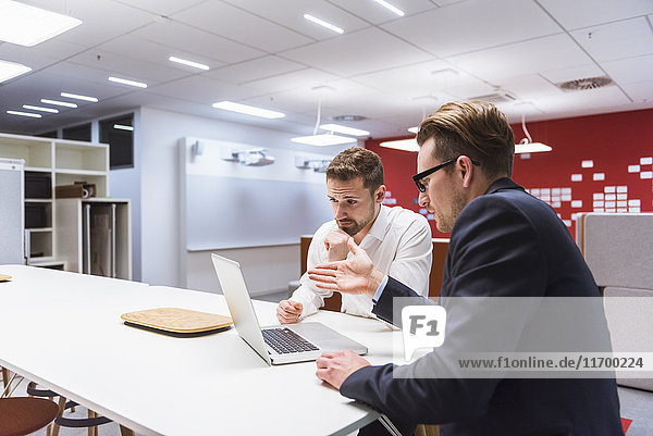 Zwei Geschäftsleute sitzen in einem modernen Büro und diskutieren vor dem Laptop.