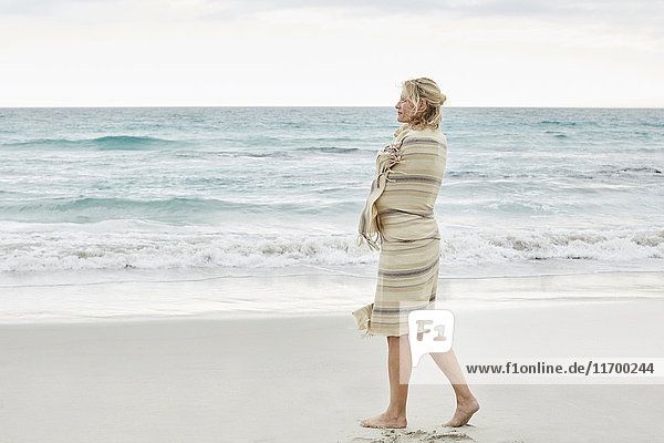 Reife Frau genießt das Meer,  eingehüllt in eine Decke