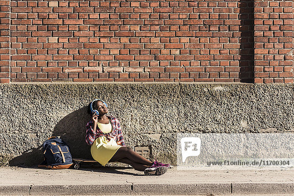 Junge Frau sitzt auf dem Boden und hört Musik mit Kopfhörern.