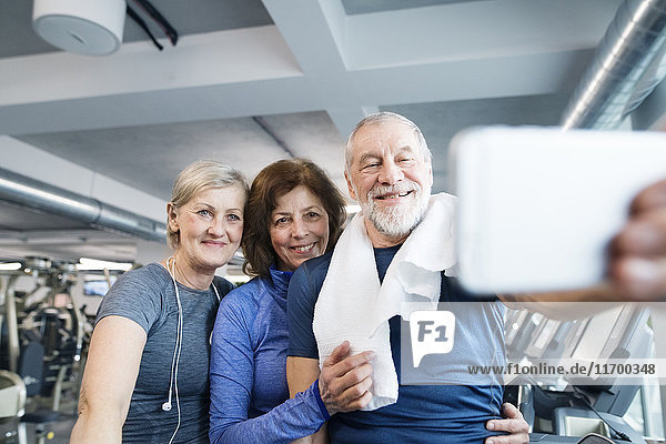 Gruppe von fit Senioren im Fitnessstudio  die nach dem Training einen Selfie mit dem Smartphone nehmen.