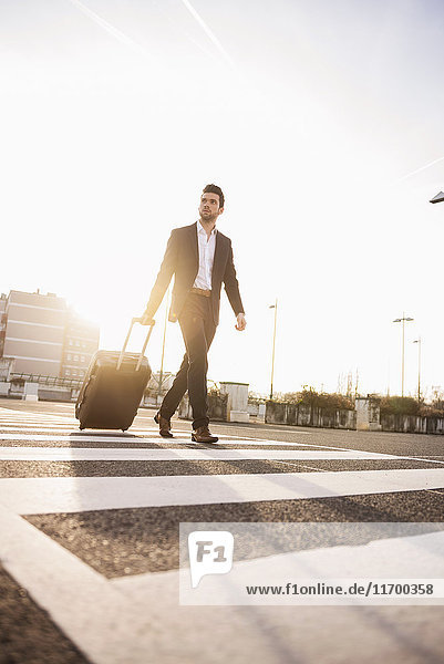 Businessman with rolling suitcase at sunset