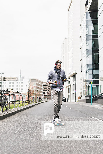Businessman skateboarding while using smartphone and earphones