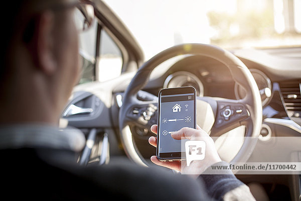 Man in car adjusting devices at home via smartphone