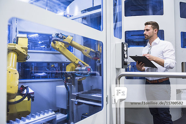 Man taking notes at robotics machine in factory shop floor