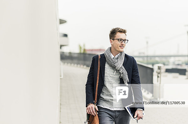 Young businessman walking in the street  carrying digital tablet and ear phones
