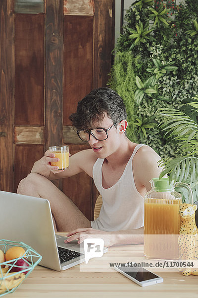 Young man using laptop and drinking orange juice at home