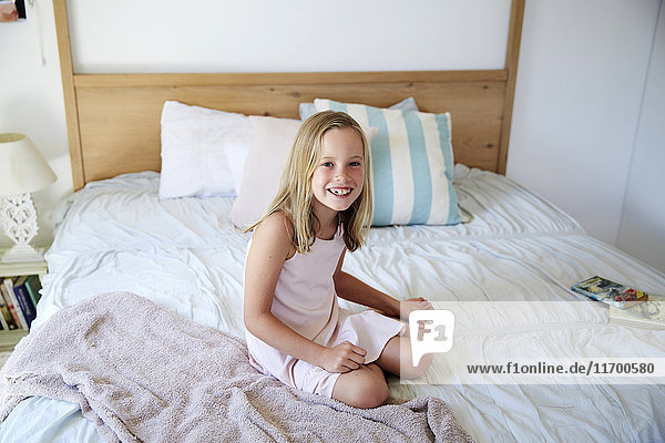Porträt eines lächelnden kleinen Mädchens  das zu Hause auf dem Bett sitzt.