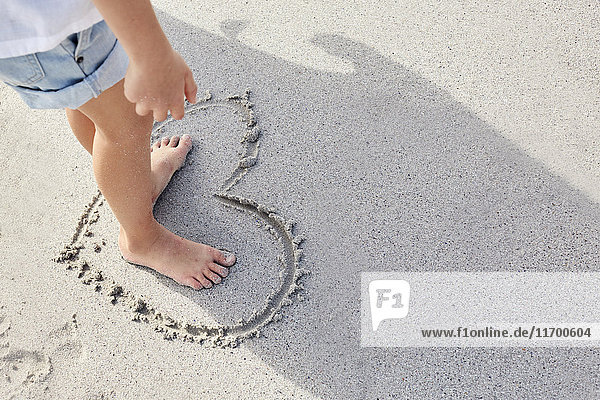 Little girl standing barefoot in a heart on sand