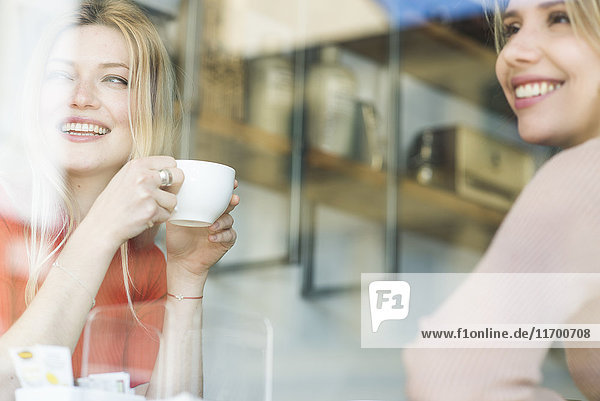 Zwei lächelnde junge Frauen in einem Café  die aus dem Fenster schauen.