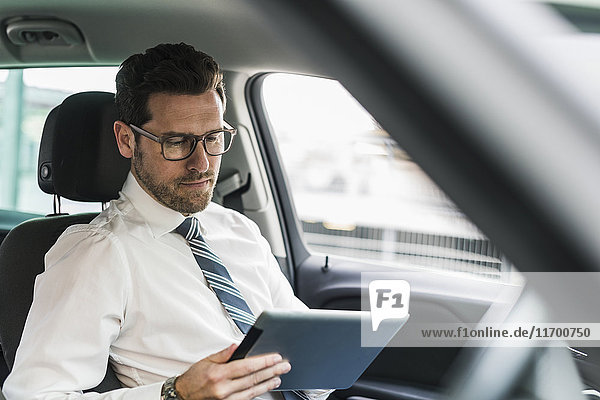 Erfolgreicher Geschäftsmann sitzend im Auto mit digitalem Tablett