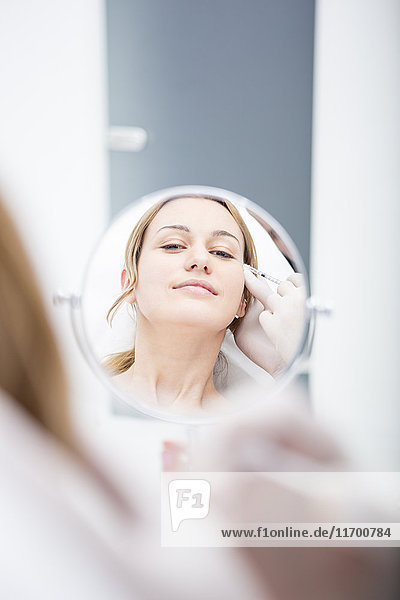 Aesthetic surgery  woman looking in mirror receiving injection