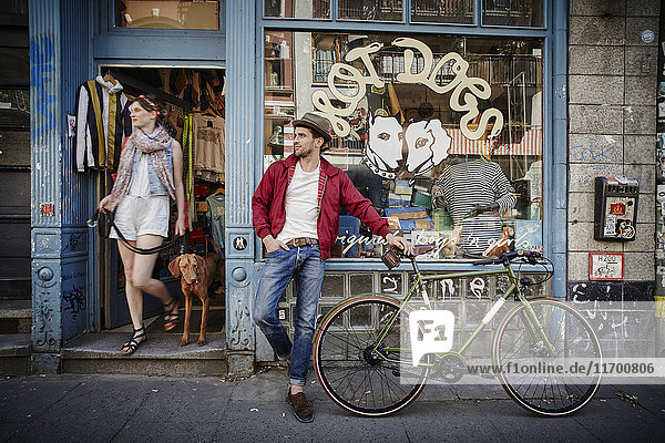 Germany  Hamburg  St. Pauli  Man with bicycle waiting in front of vintage shop  woman with dog coming out