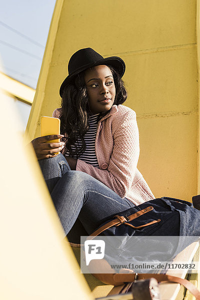 Junge Frau auf der Brücke sitzend mit dem Smartphone
