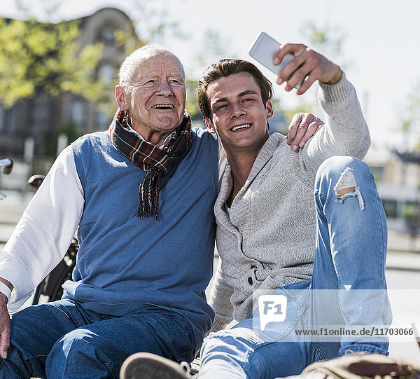 Senior-Mann und erwachsener Enkel auf einer Bank mit einem Selfie