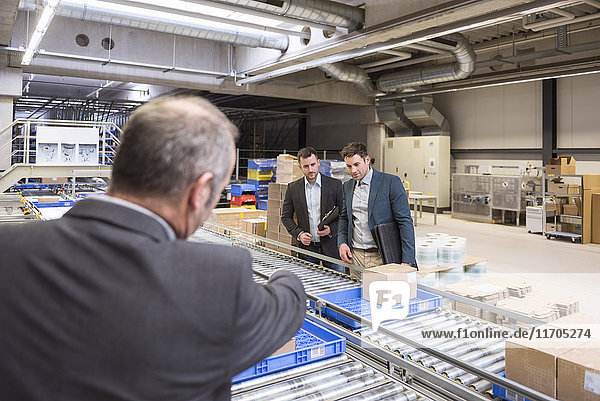 Three businessmen at conveyor belt in factory