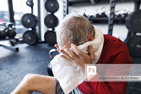 Exhausted senior man sitting on the floor after working out in gym