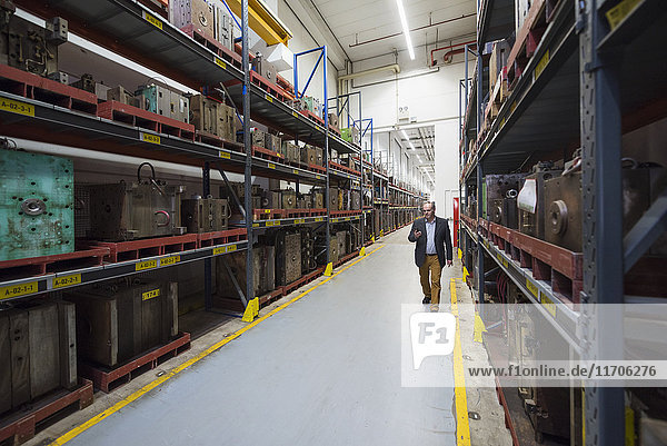 Businessman walking in factory storehouse looking at cell phone