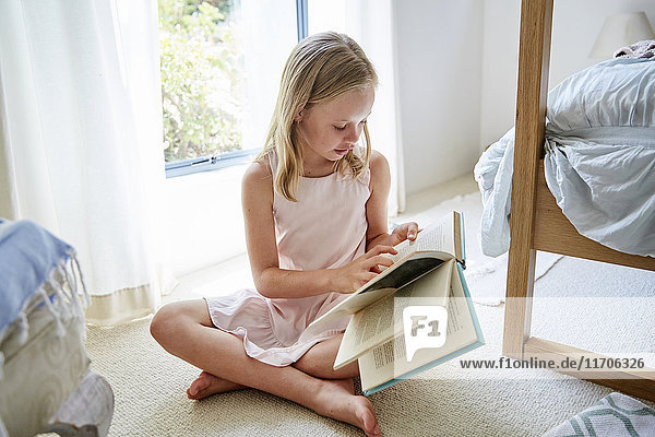 Little girl sitting on the floor at home reading a book