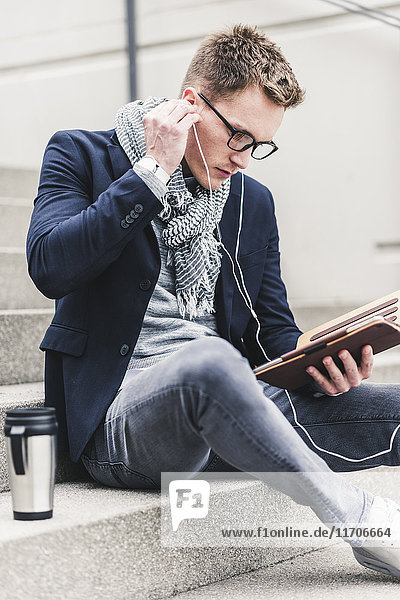 Ein junger Geschäftsmann sitzt auf einer Treppe und benutzt ein digitales Tablett.