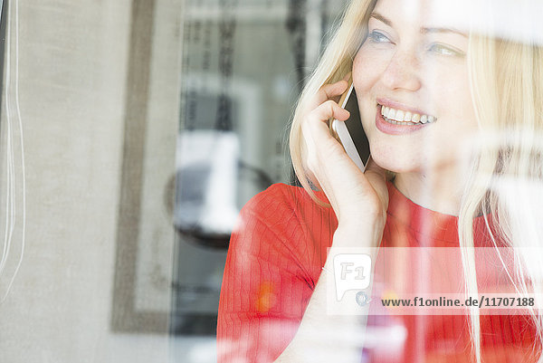 Lächelnde junge Frau am Telefon  die aus dem Fenster schaut.