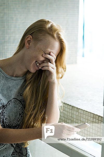 Junge Frau hält Smartphone  lachend