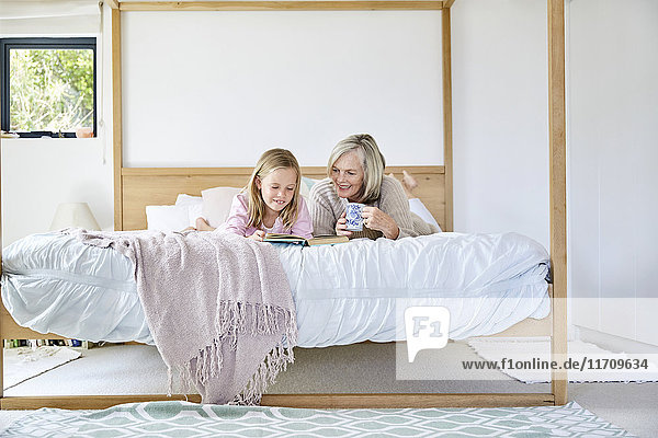 Kleines Mädchen auf dem Bett liegend mit ihrer Großmutter  die ein Buch liest.