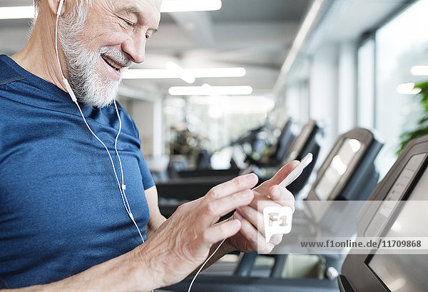 Senior Mann mit Smartphone und Kopfhörer im Fitnessstudio