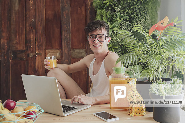 Junger Mann mit Laptop und Orangensaft zu Hause