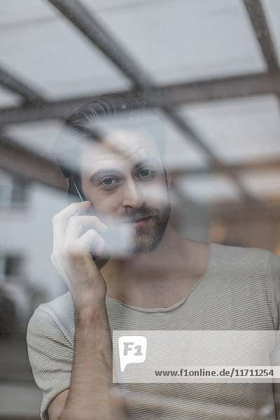 Porträt eines jungen Mannes am Telefon hinter der Fensterscheibe
