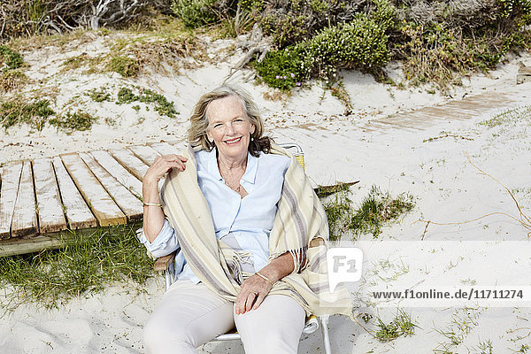 Senior woman sitting on the beach  looking at camera