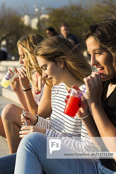 Drei junge Frauen mit Erfrischungsgetränken bei Sonnenuntergang