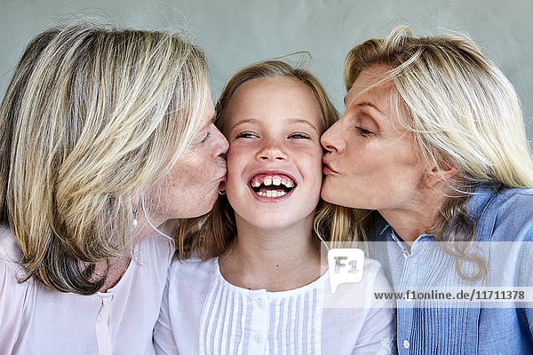 Portrait of happy little girl kissed by mother and grandmother