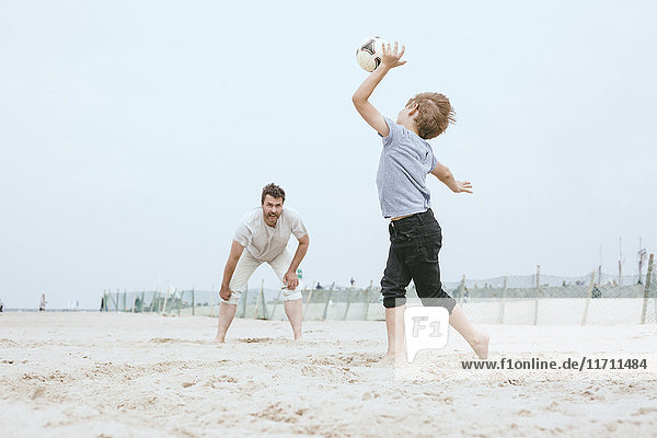Father and little son playing with ball on the beach