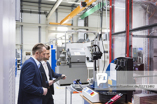 Two businessmen in factory shop floor examining machine