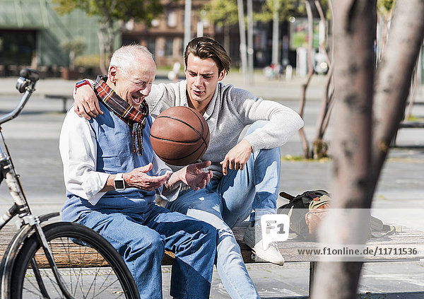 Senior Mann und erwachsener Enkel mit Basketball auf einer Bank im Gespräch