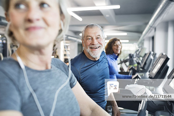 Gruppe von fit Senioren auf Laufbändern im Fitnessstudio  Mann lächelt